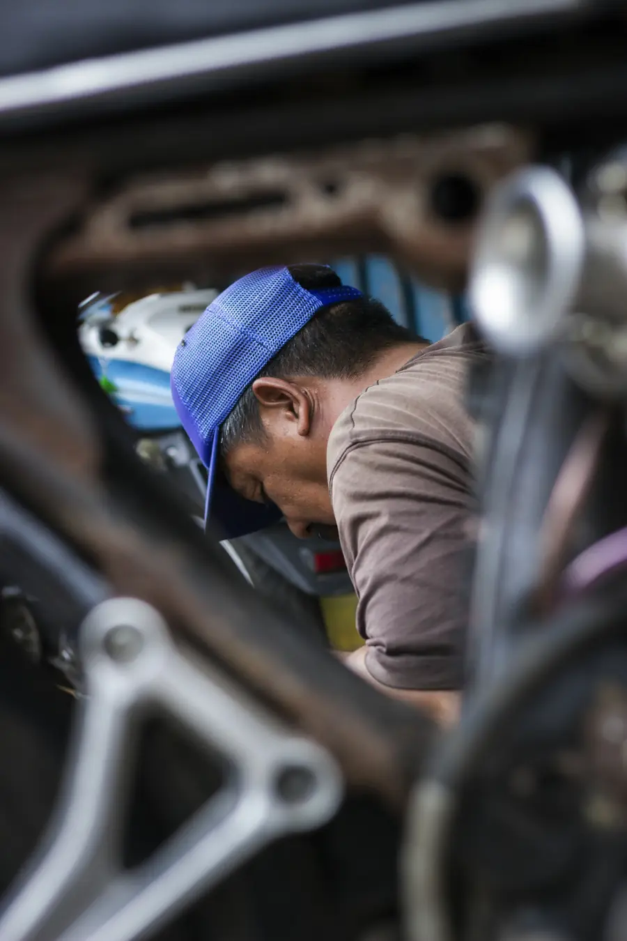 Montir bertopi biru mengerjakan kendaraan di bengkel